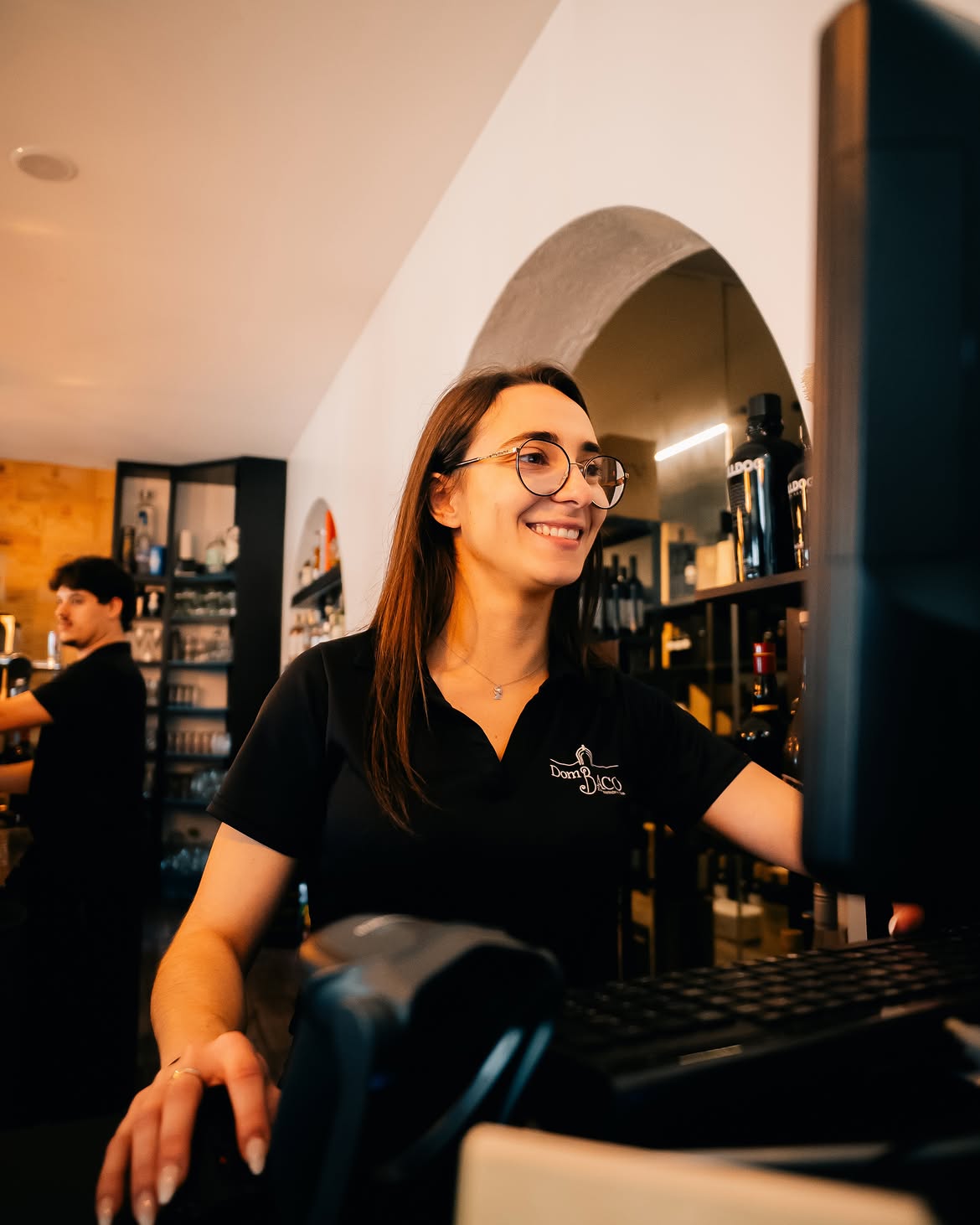Funcionária sorridente no balcão do bar do Dom Baco