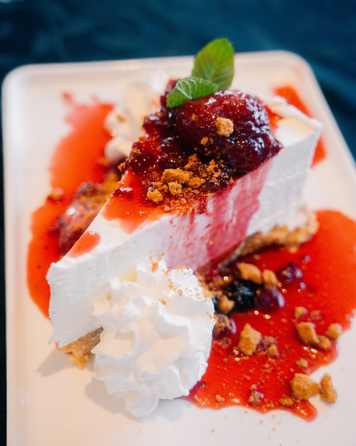 Fatia de cheesecake com calda de frutas vermelhas, chantili e hortelã