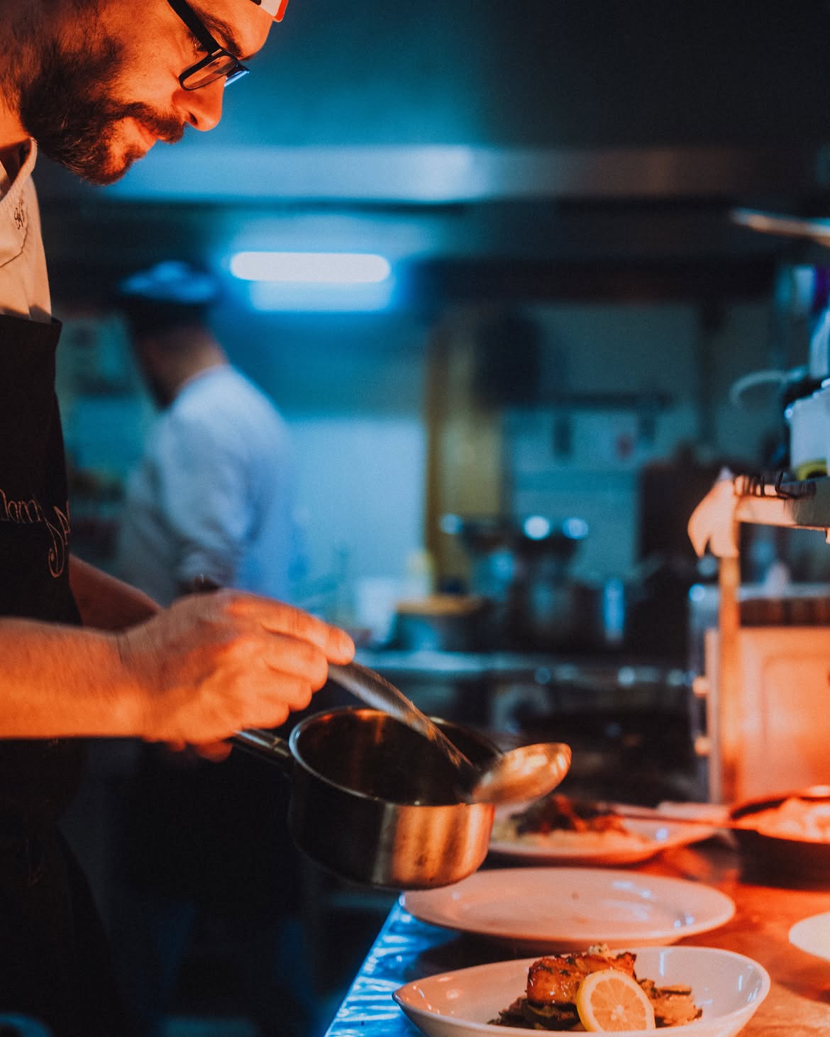 Chef montando o prato com atenção aos detalhes, na cozinha em tons quentes