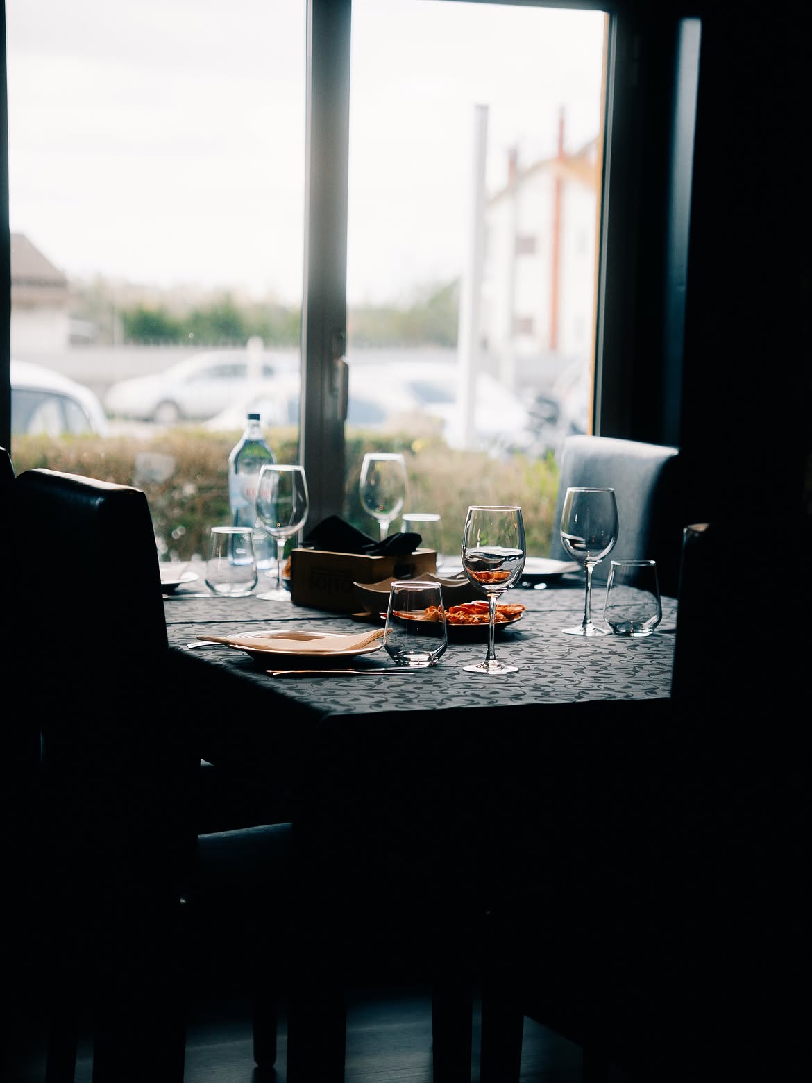 Mesa posta junto à janela, com taças de vinho e aperitivos