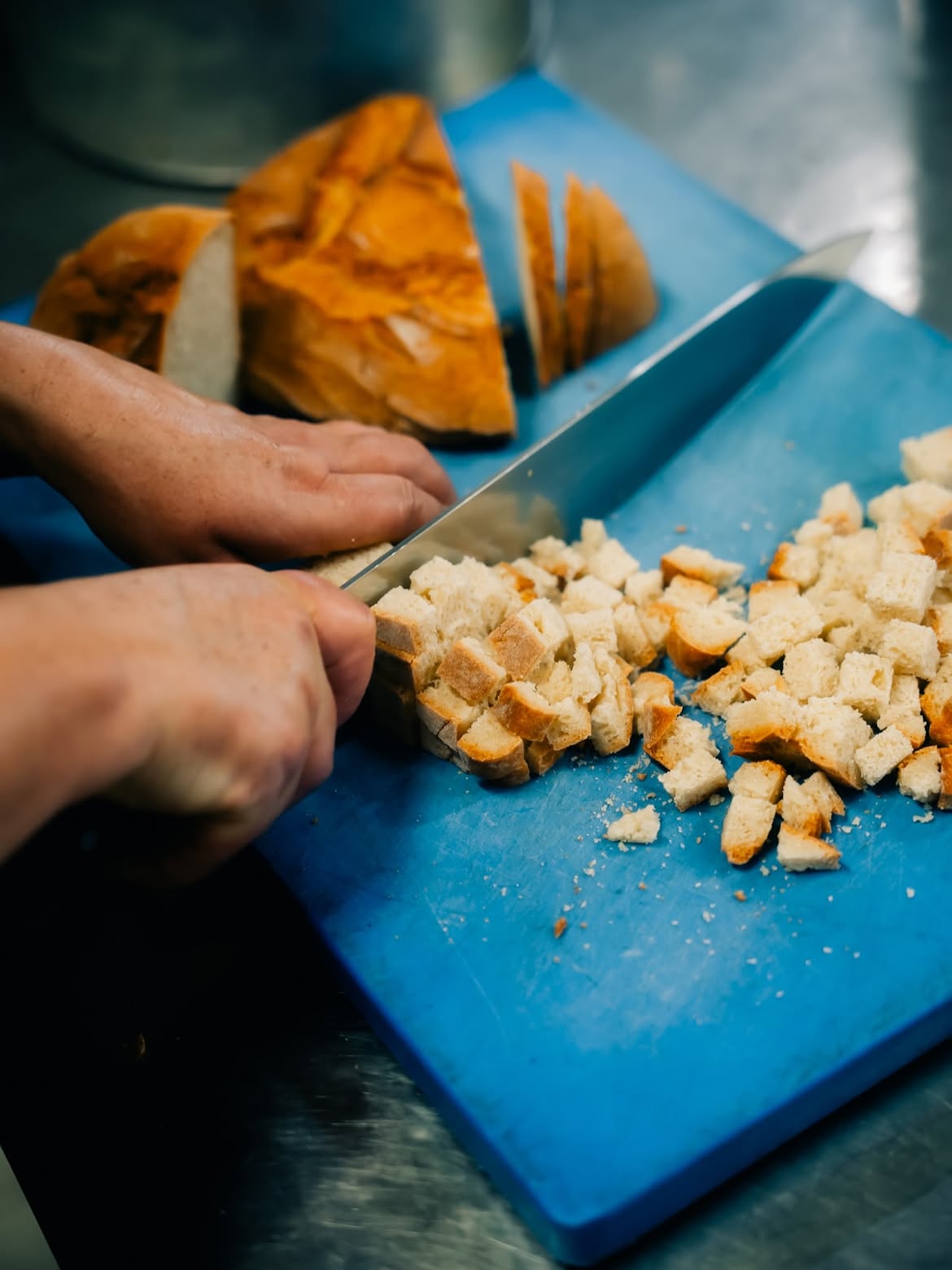 Mãos cortando pão rústico em cubos na cozinha