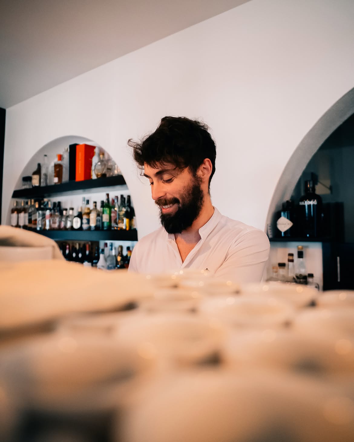 Barista sorridente atrás do balcão, ao lado da adega do bar